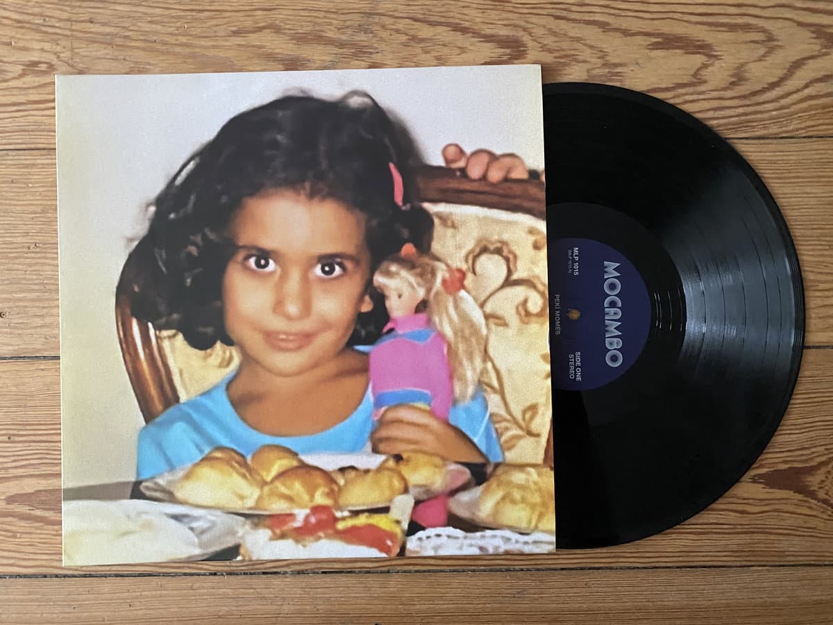 Vinyl record for Peki Momés - Peki Momés with a cover featuring a young girl and a doll on a wooden surface